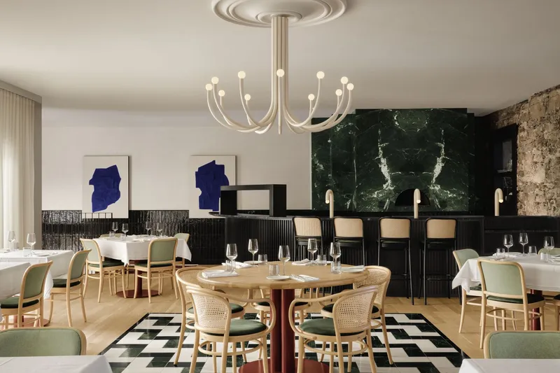 Restaurant dining room with fluted chandelier, cane chairs and dark green marble wall behind the bar