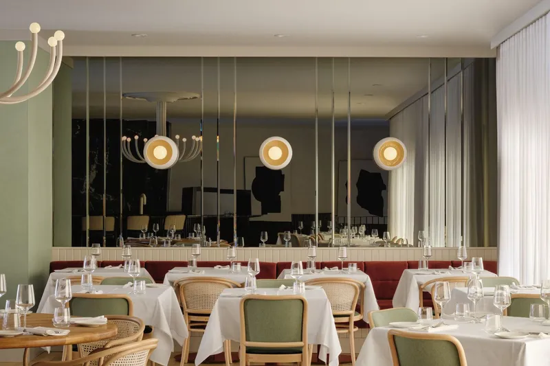 Mirrored wall reflecting pendant lights and white-clothed tables in the dining area
