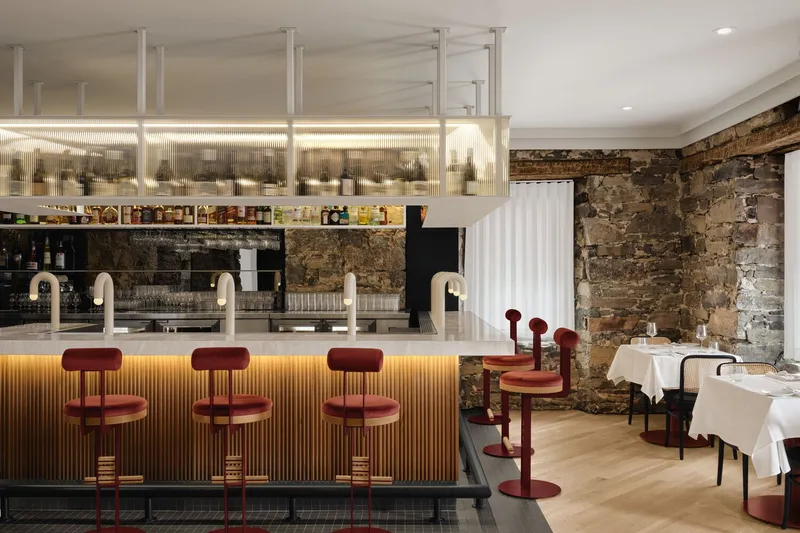 Bar with ribbed timber front, backlit glass shelves and weathered stone wall at the rear