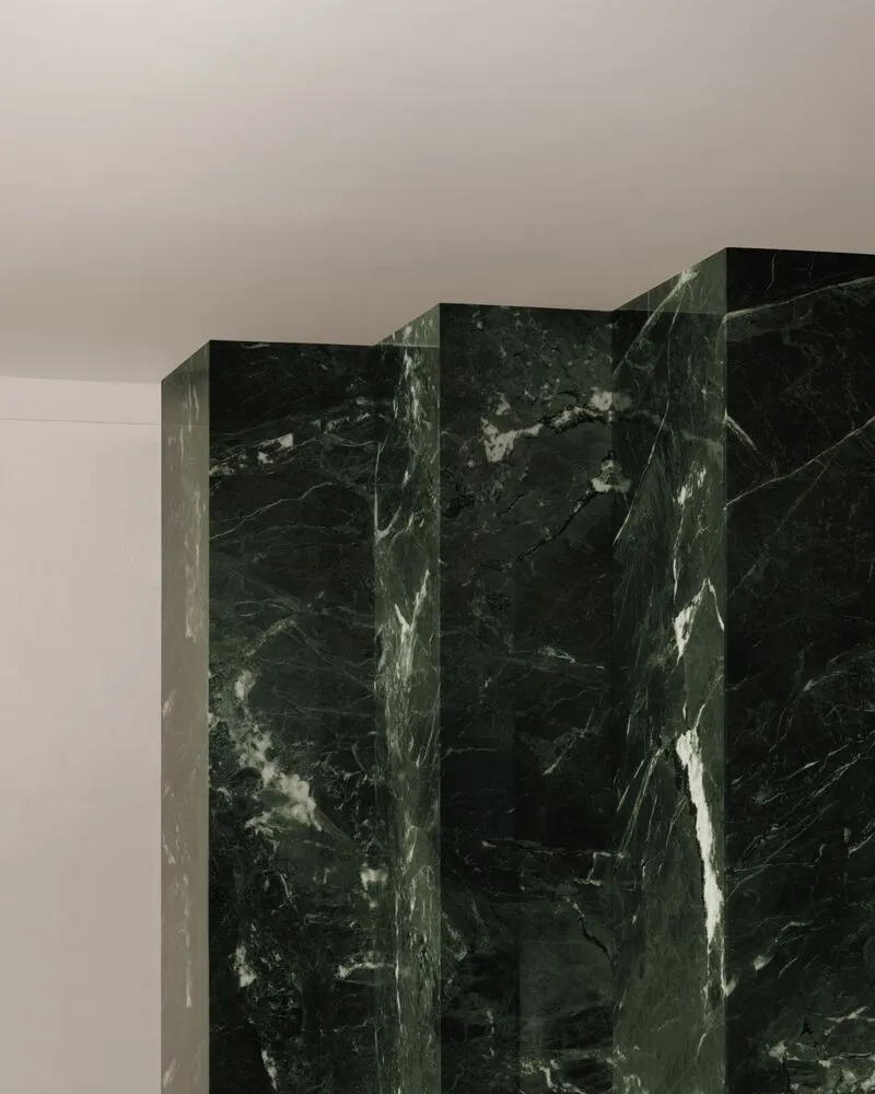 Close-up of a dark green veined marble wall meeting the ceiling in soft shadow