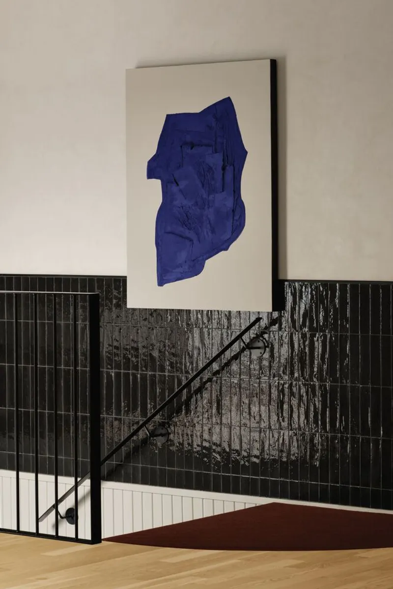 Staircase with black metal railing beside dark tiled wall and a blue artwork on beige surface
