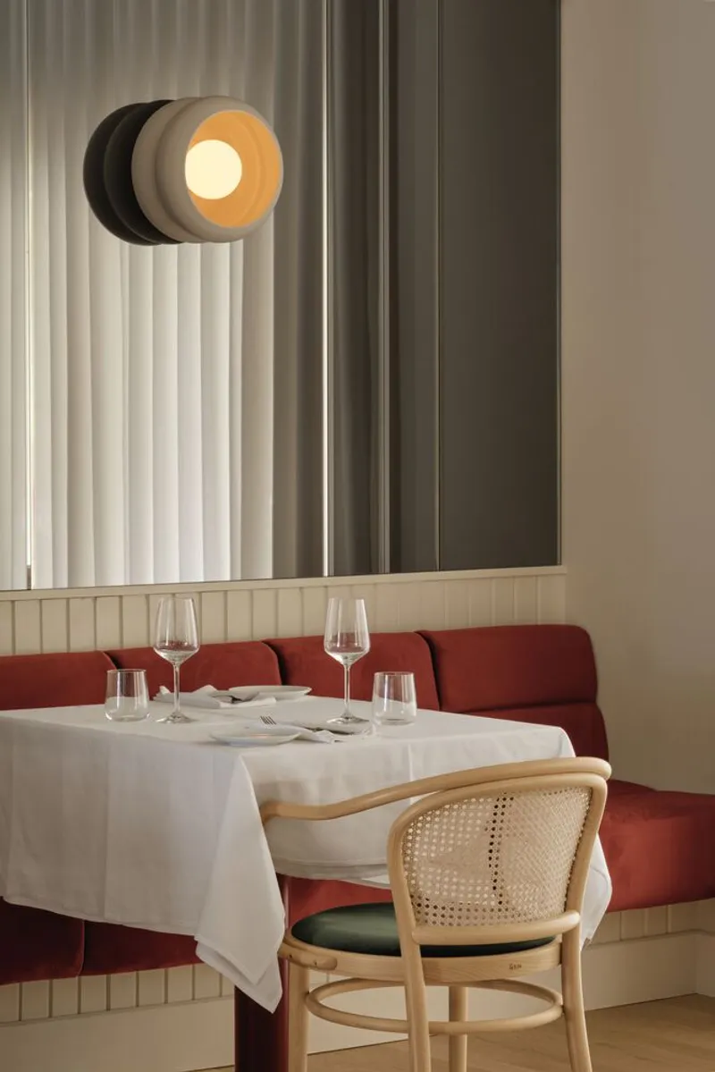 Detail of circular wall sconce with black and amber discs above a banquette with white tablecloth