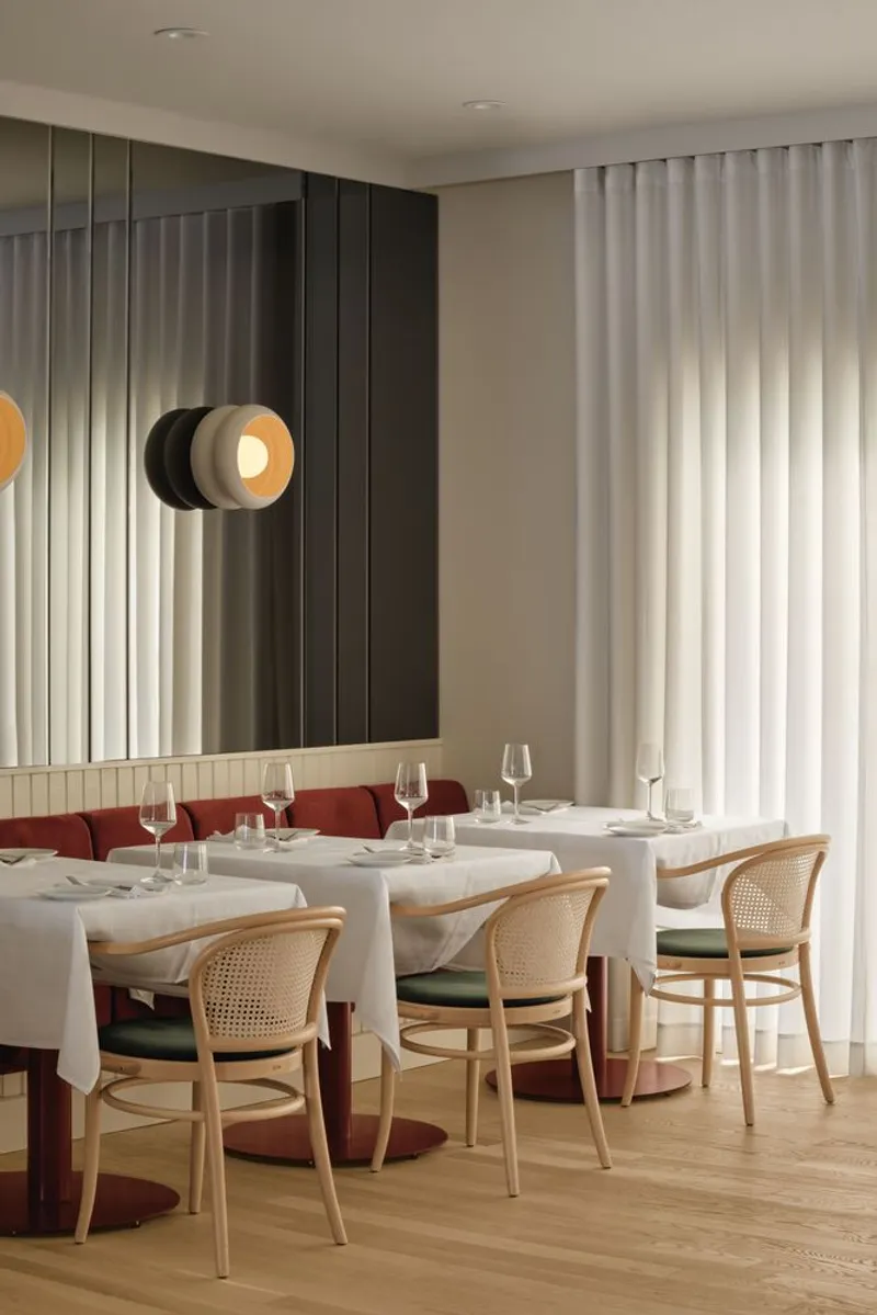 Dining area with cane-backed chairs and layered circular wall sconce reflected in fluted glass panels