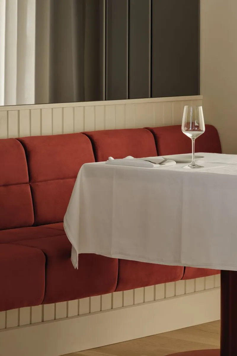 Corner view of upholstered red banquette with fluted cream wainscoting and a single wine glass