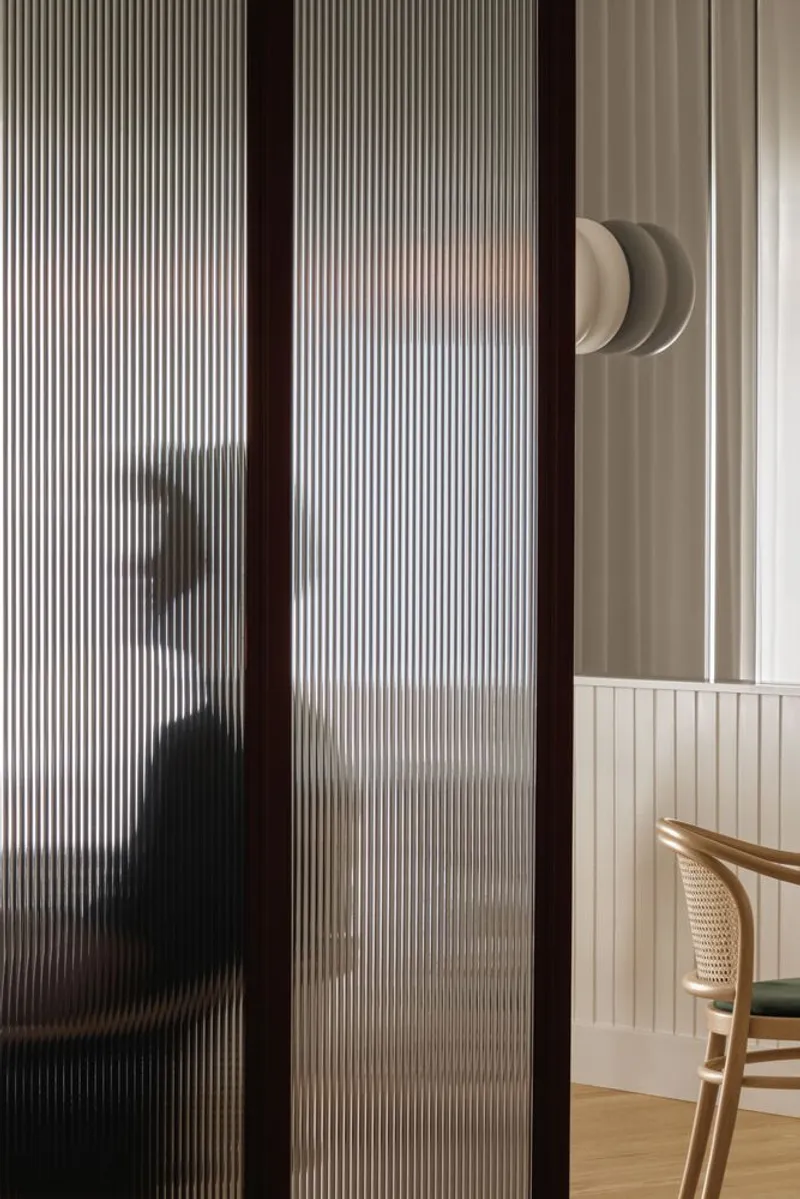 Translucent fluted glass sliding door with dark timber frame revealing a silhouette beyond