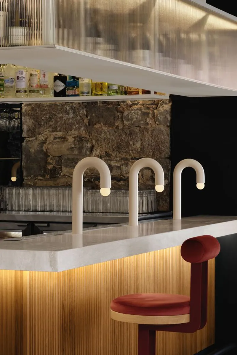 White stone countertop with three curved tap fixtures in front of exposed rubble stone wall