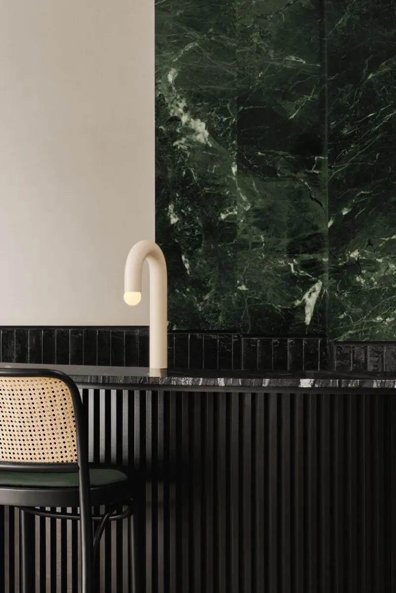 Curved wall sconce beside green veined marble panel above fluted black timber wainscoting