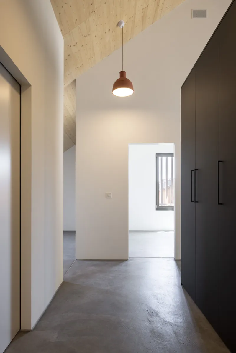 Narrow corridor with polished concrete floor and red pendant light beneath a plywood ceiling