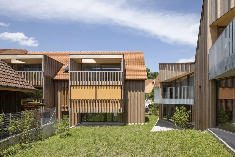 Timber-clad volumes with vertical slat screens facing a shared lawn under a blue sky
