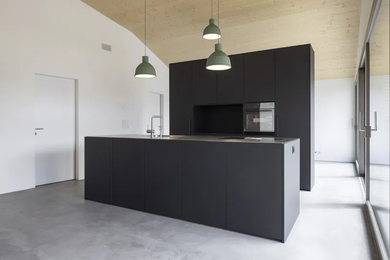 Black kitchen island and cabinetry wall with concrete floor and sliding glass doors to garden