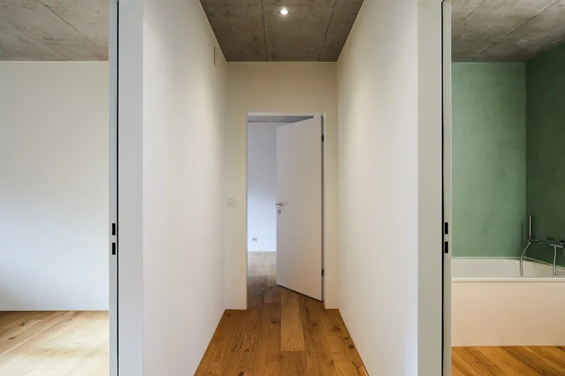 Hallway sequence with timber and concrete ceilings connecting white-walled rooms with oak flooring