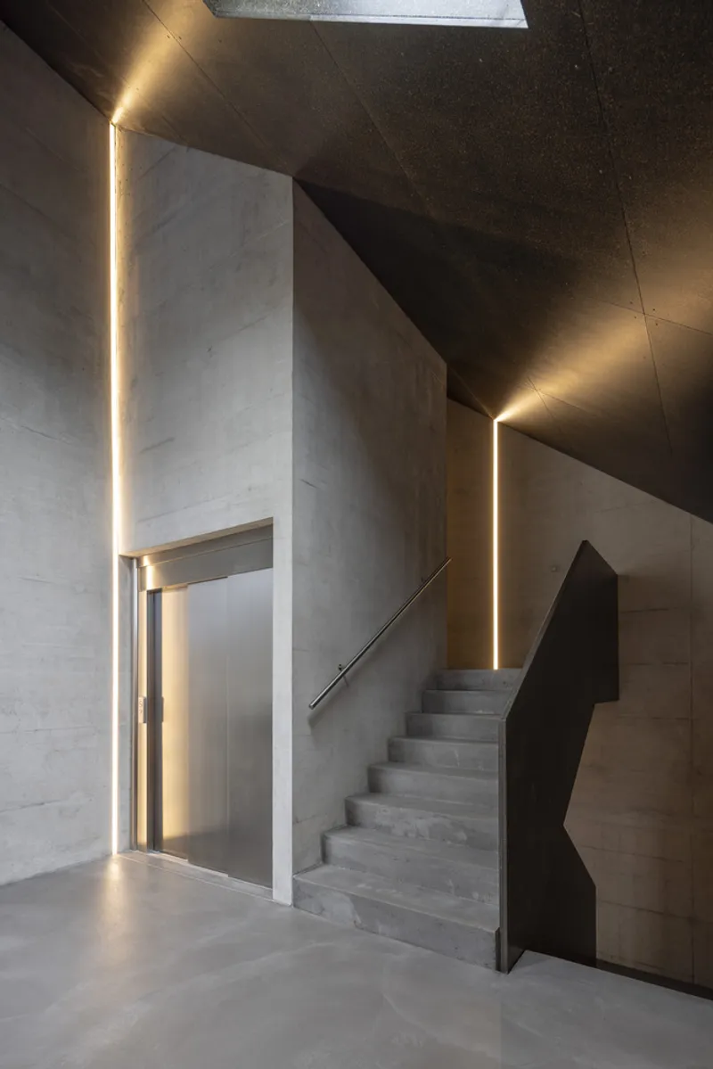 Concrete staircase with LED-lit vertical slots framing the doorway and ascent in warm light