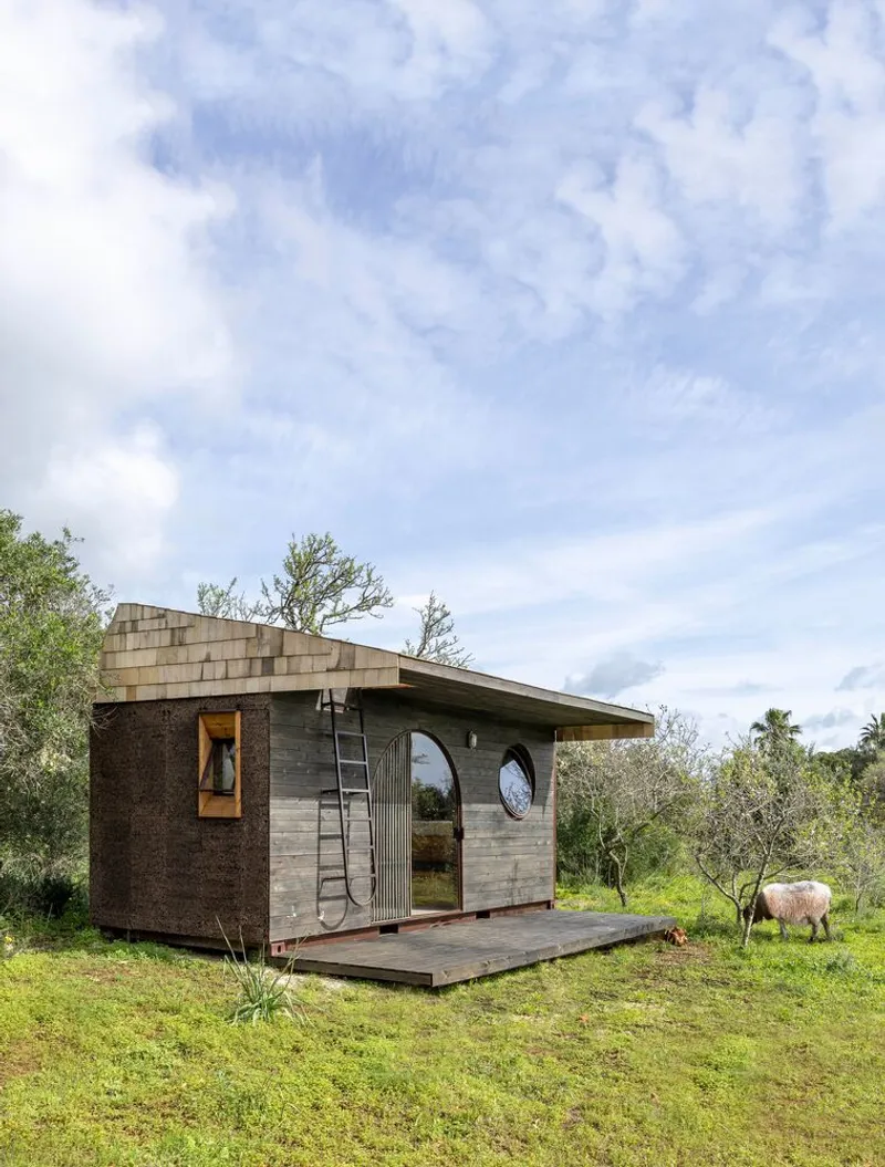 Exterior view showing the cork-clad wall and angled roof with a sheep grazing beside the deck