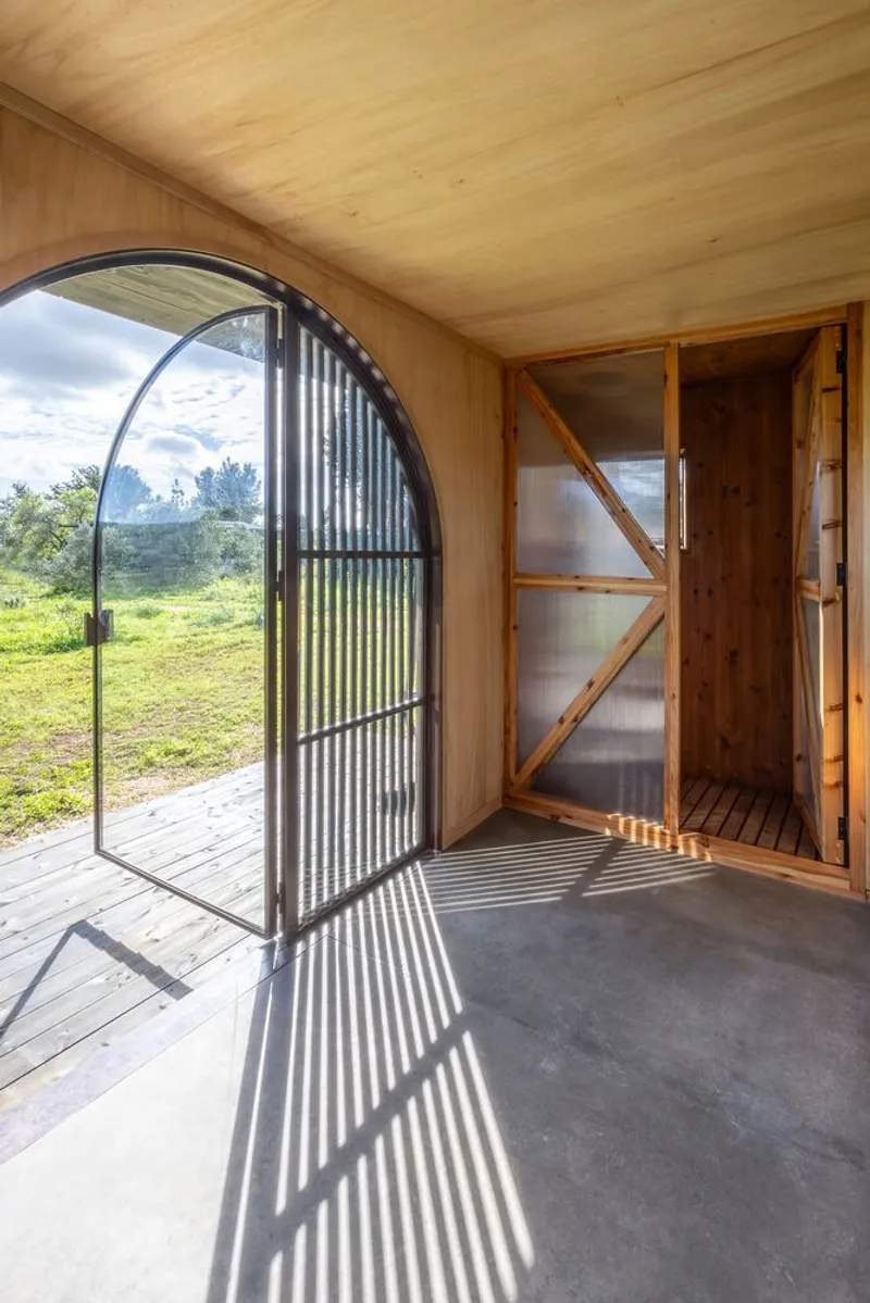Arched corrugated metal door swung open casting striped shadows across the concrete floor and plywood ceiling