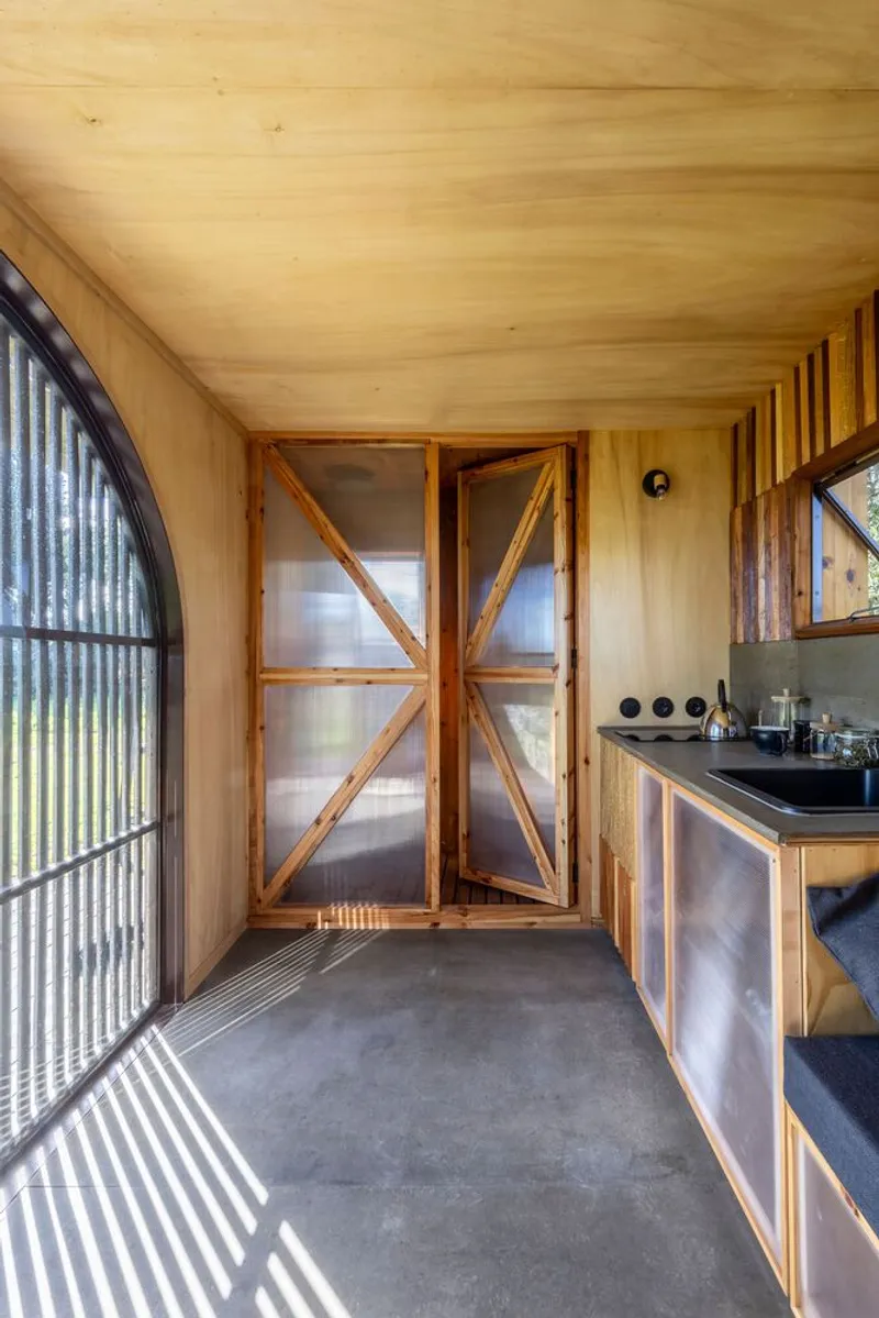 Interior corridor with plywood walls and ceiling showing diagonal braced doors and a compact kitchenette counter