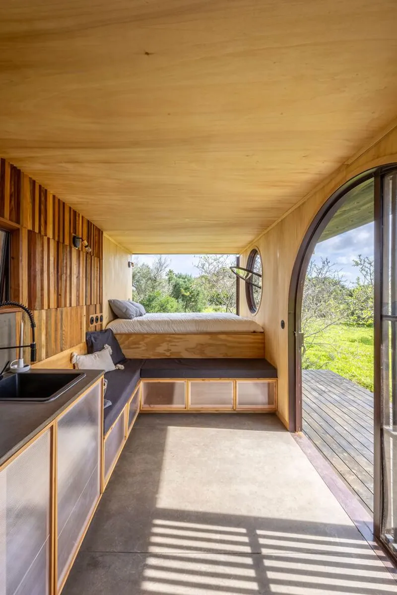 Interior with plywood ceiling, vertical slat wall, built-in bed platform and circular window overlooking landscape