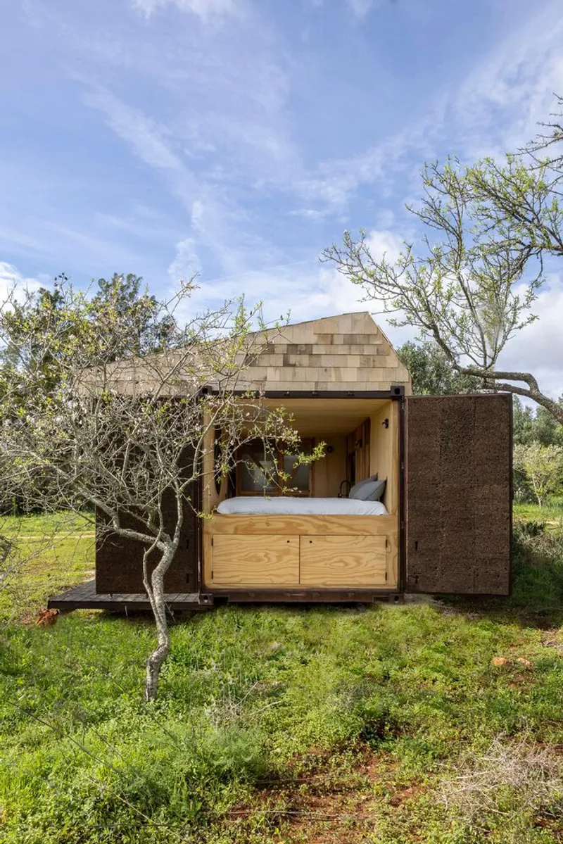 Open timber bedroom pod under the cantilevered roof framed by bare trees and grass