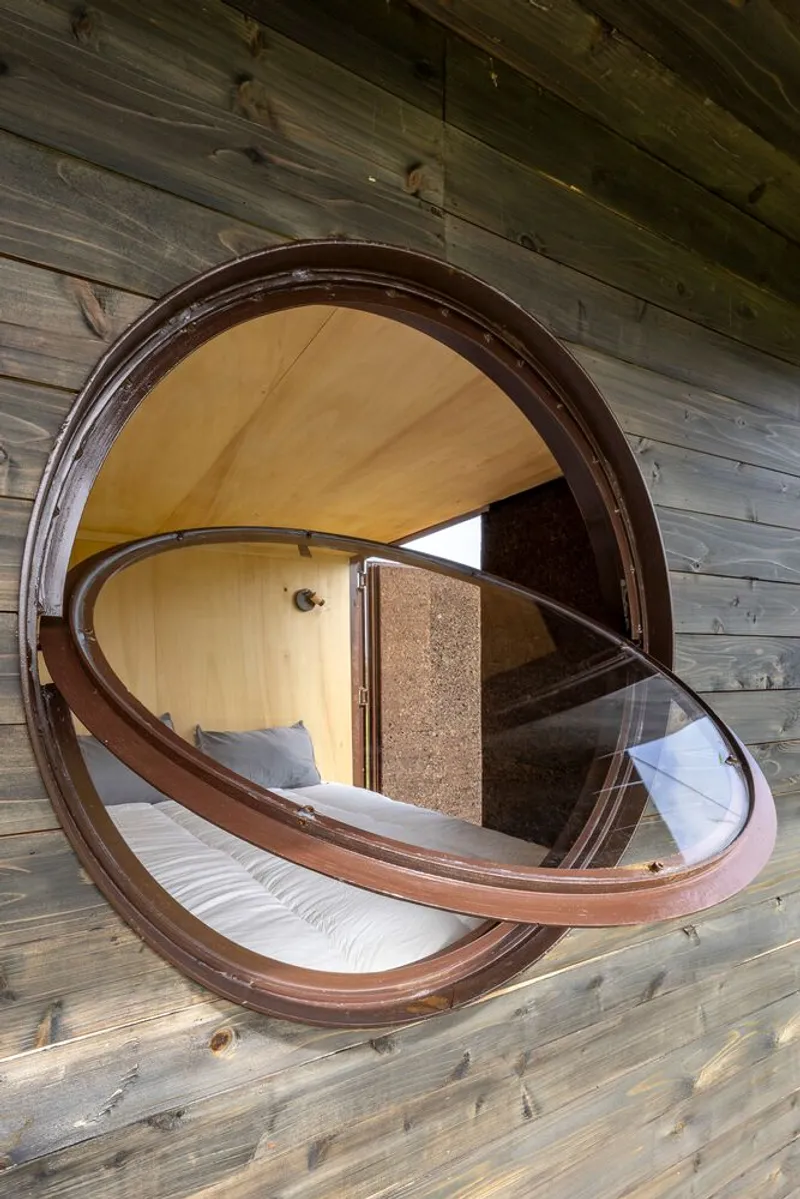Circular pivot window open from timber deck revealing plywood ceiling and cork wall inside