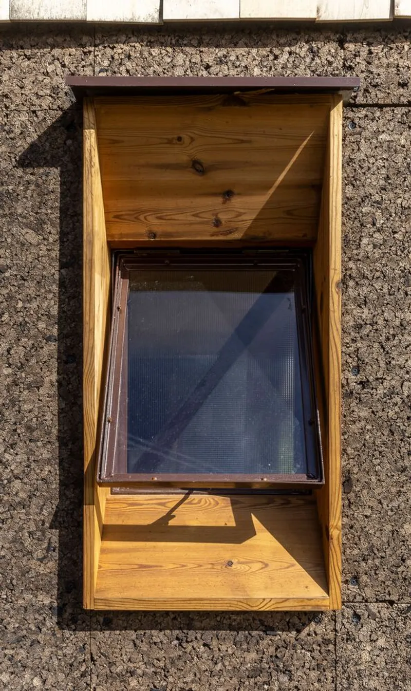 Detail of timber-framed window inset in the textured cork facade with diagonal shadow