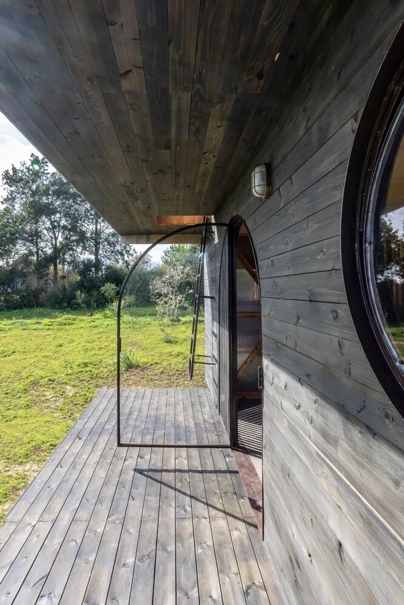 Covered porch with arched steel-framed door opening to the landscape at dusk