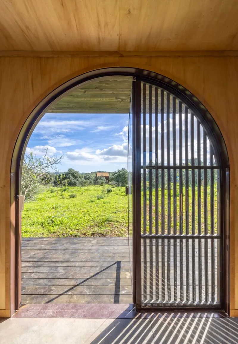 Interior view through arched door with slatted screen looking out to the olive field