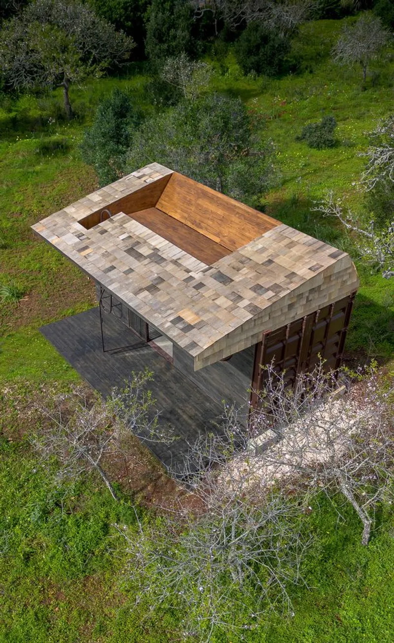 Aerial view of the square pavilion with patchwork stone roof and central timber-lined courtyard opening