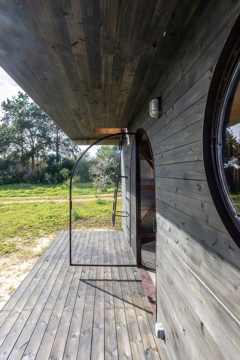 Covered timber deck with arched doorway opening to a grassy field in afternoon light