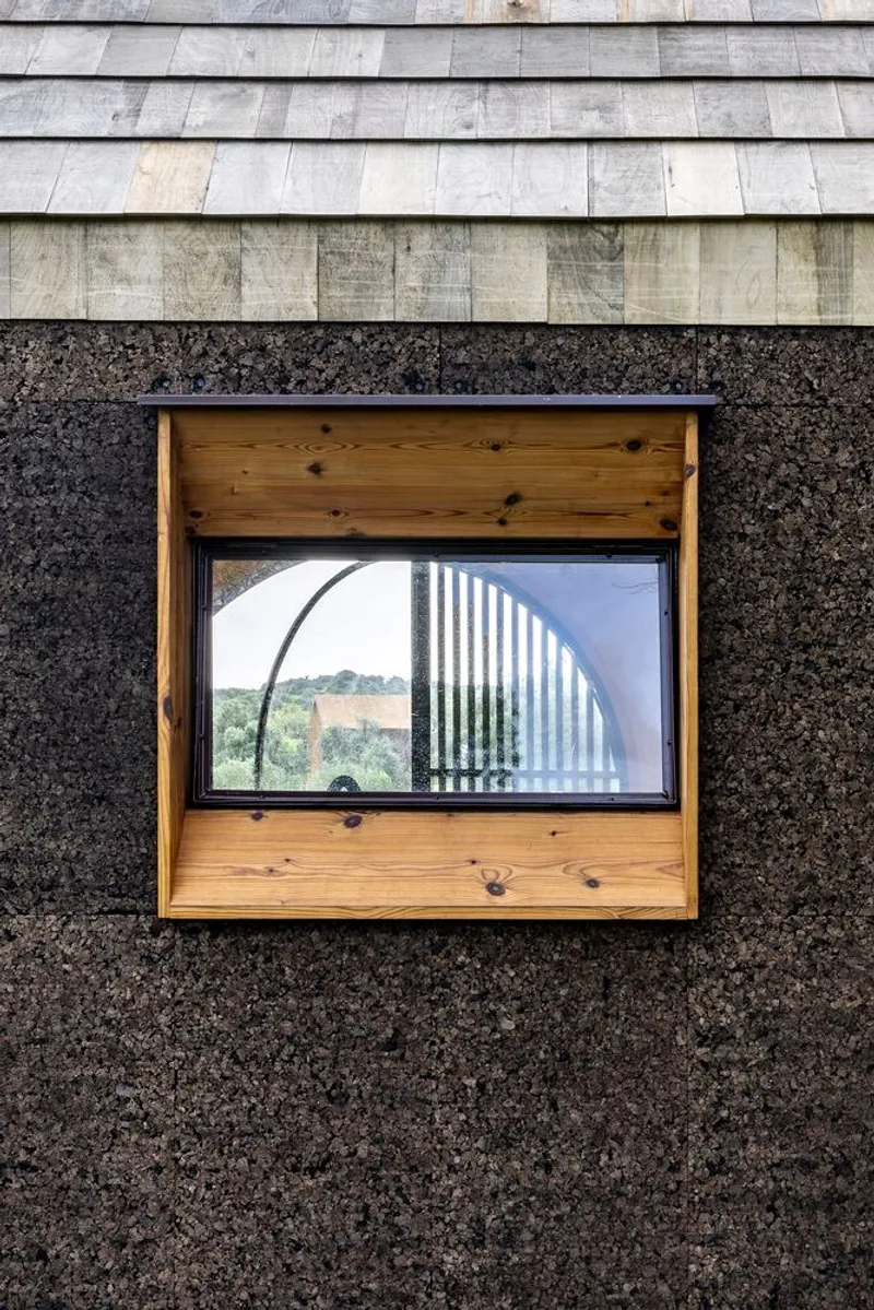 Timber-framed window in cork wall reflecting interior arched door and distant landscape