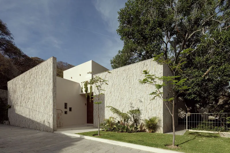 Street view of the white brick facade with planted lawn and young trees in afternoon light