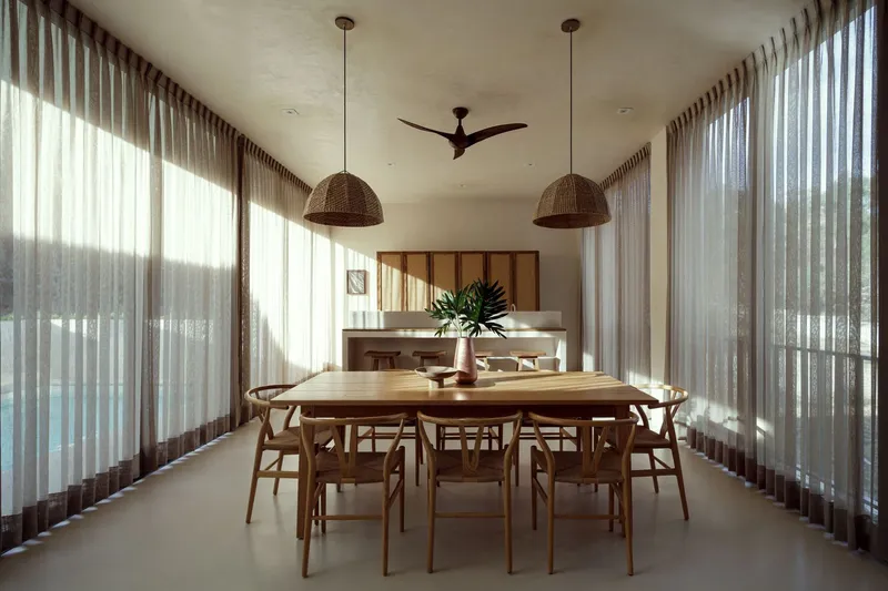 Dining room with timber table and woven pendant lights beneath sheer curtains filtering daylight