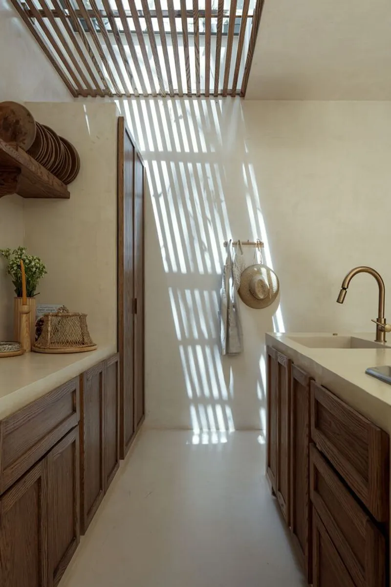 Galley kitchen with timber cabinetry and slatted overhead screen casting striped shadows on the wall