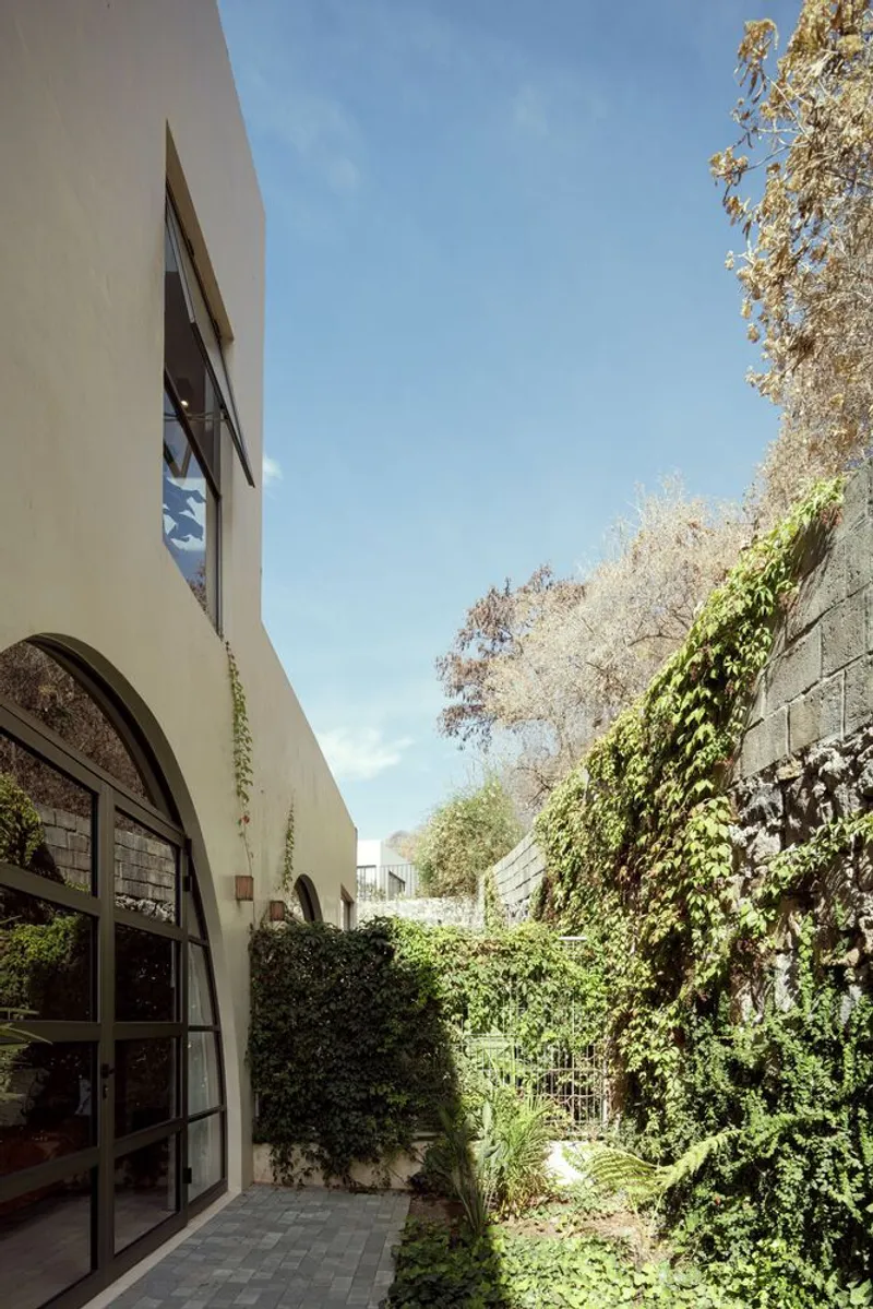 Exterior passage between arched glazed doors and a vine-covered hillside retaining wall