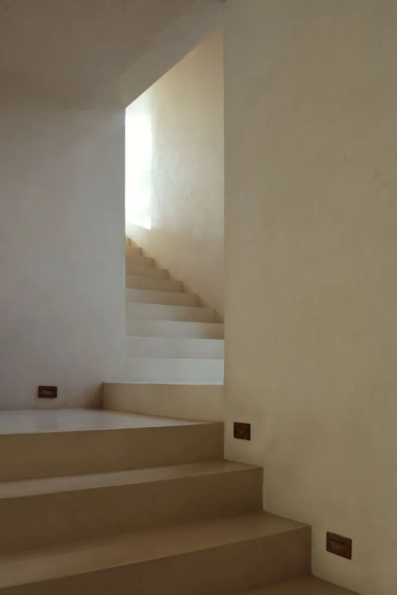 Cantilevered stone staircase turning around a white plaster wall with small recessed floor lights