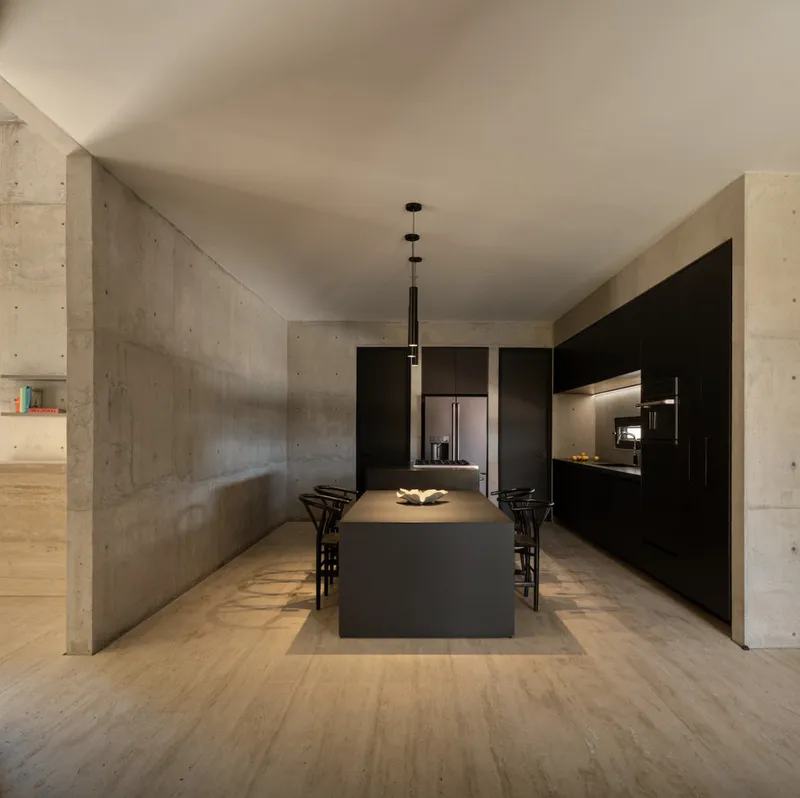 Kitchen with black island and cabinetry set between board-formed concrete columns under pendant lighting