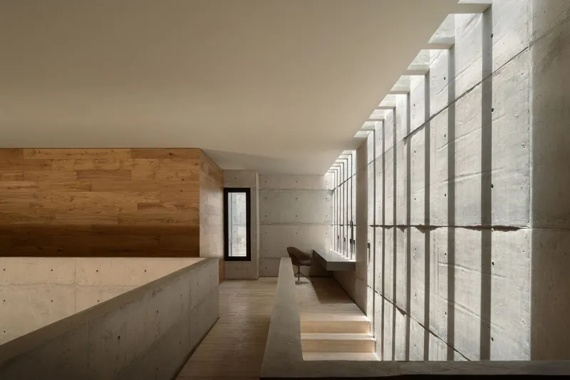 Upper-level corridor with rhythmic concrete fins creating vertical shadow patterns along the glass wall