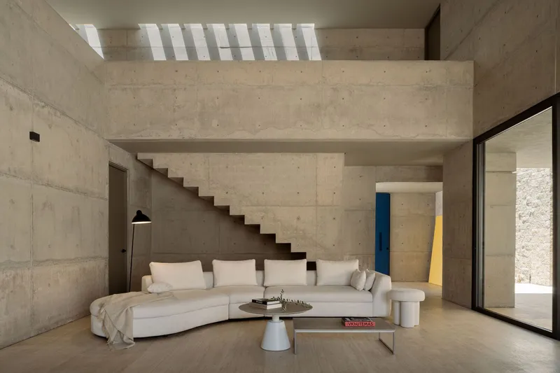 Double-height living room with cantilevered concrete staircase beneath a slatted skylight casting shadow stripes
