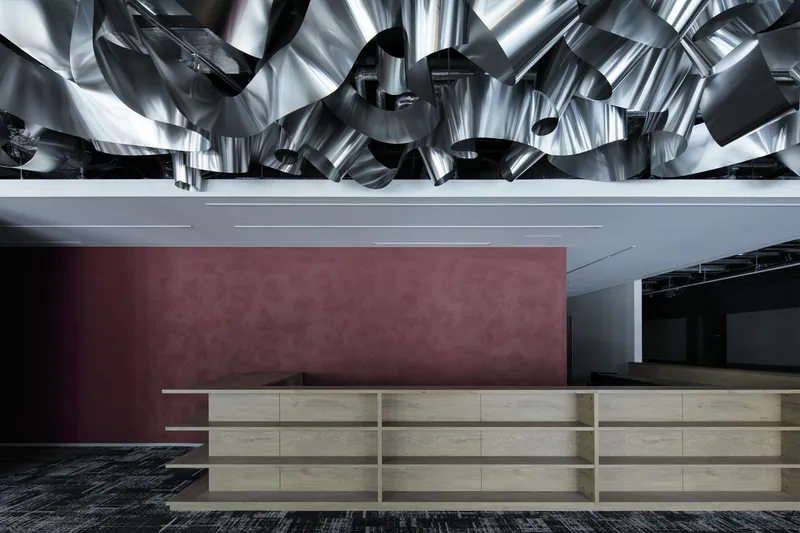 Horizontal wood-paneled reception counter against a maroon plaster wall beneath a reflective metallic ceiling