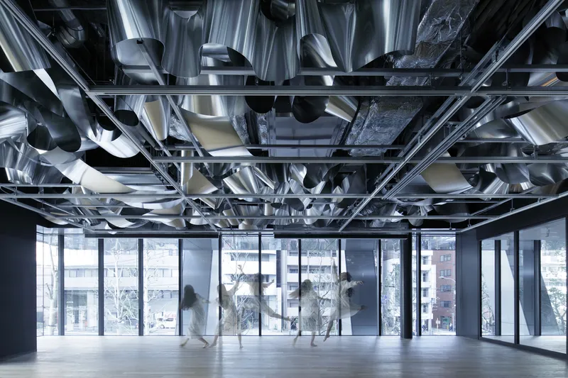 Open interior space with people in motion beneath suspended folded metal ceiling and exposed black structural frame