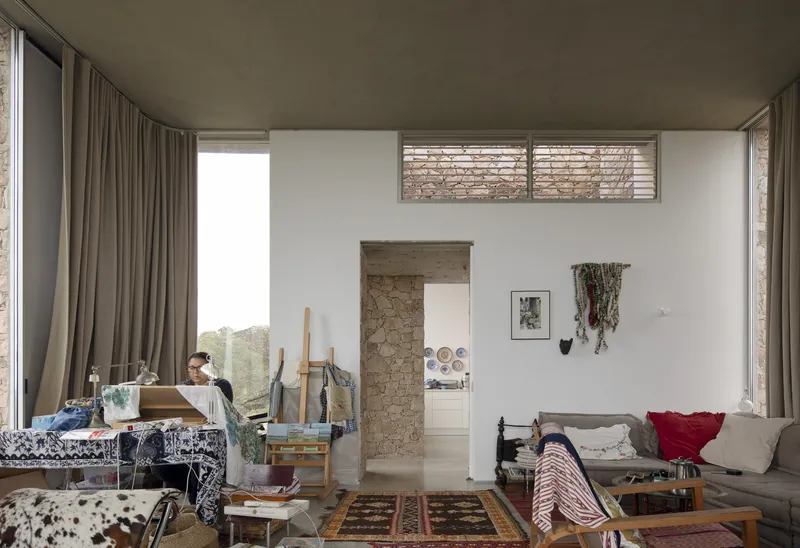 Living room interior with stone doorway, clerestory window, art studio setup and full-height curtains