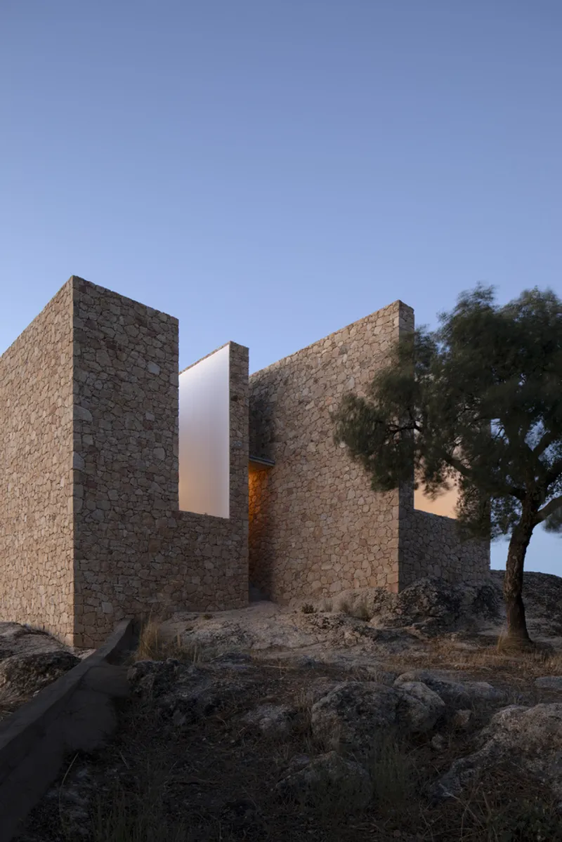 Courtyard composition of tall stone walls flanking a white tower volume at dusk