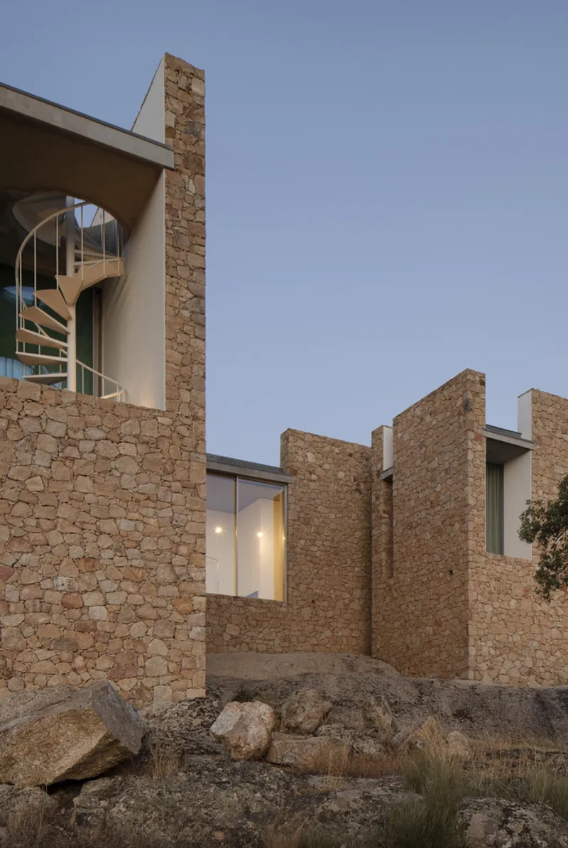 Staggered stone walls with cantilevered volumes and spiral staircase visible at dusk