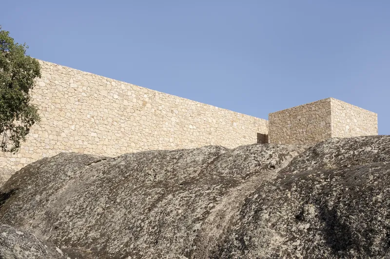 Stone volumes perched on sloped granite outcrop beneath clear sky