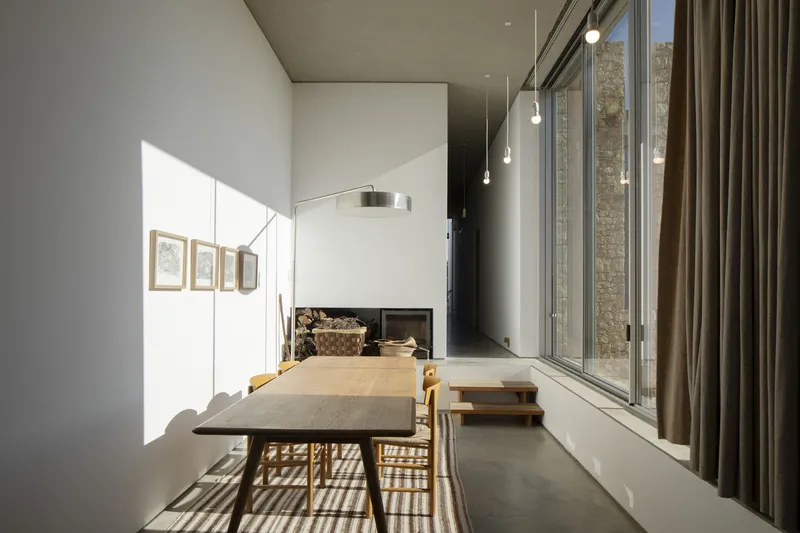 Dining space with timber table and suspended pendant lights casting shadows through glazed wall