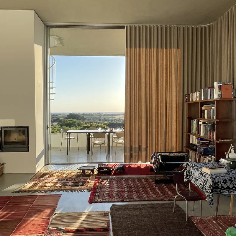 Interior with layered rugs and floor-to-ceiling curtain framing terrace view at golden hour