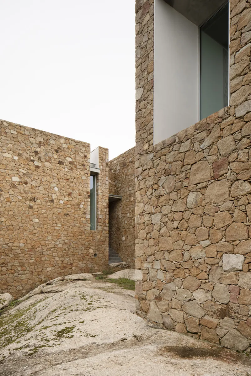 Narrow courtyard between rough stone walls with patches of grass on the sandy ground