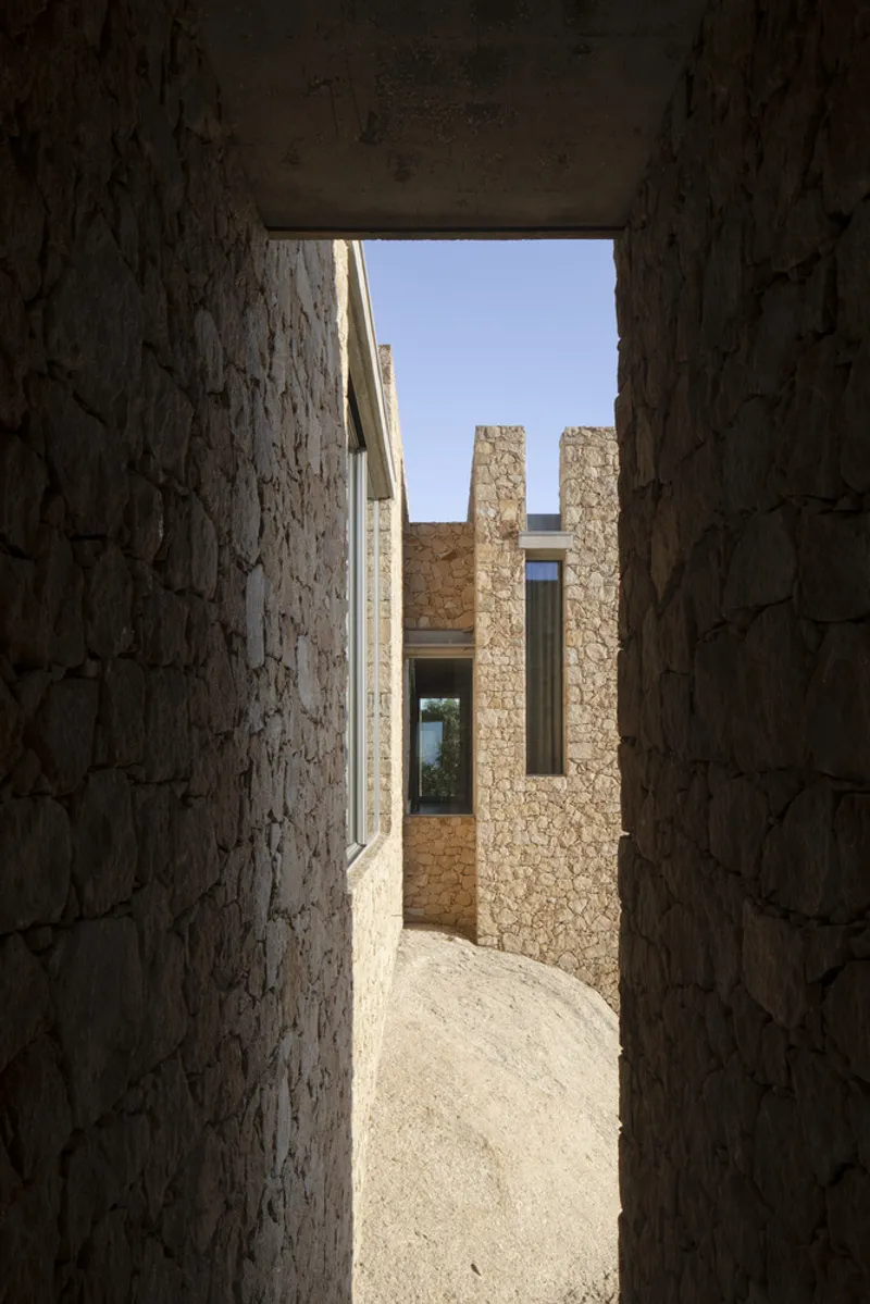View through a stone passageway toward freestanding stone walls and window openings beyond