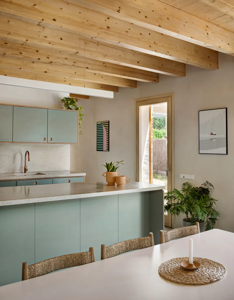 Kitchen and dining area with exposed timber beams, pale green cabinetry and door to garden