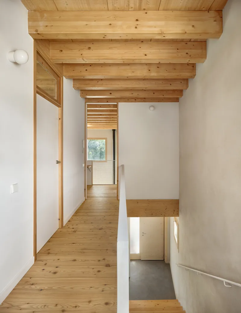 Upper level hallway with pine flooring and exposed timber beams overlooking the entry below
