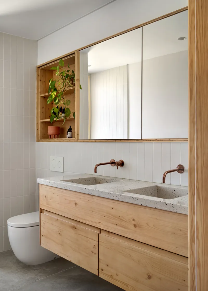 Bathroom vanity with terrazzo countertop, timber cabinetry, copper tapware and potted plant in shelf