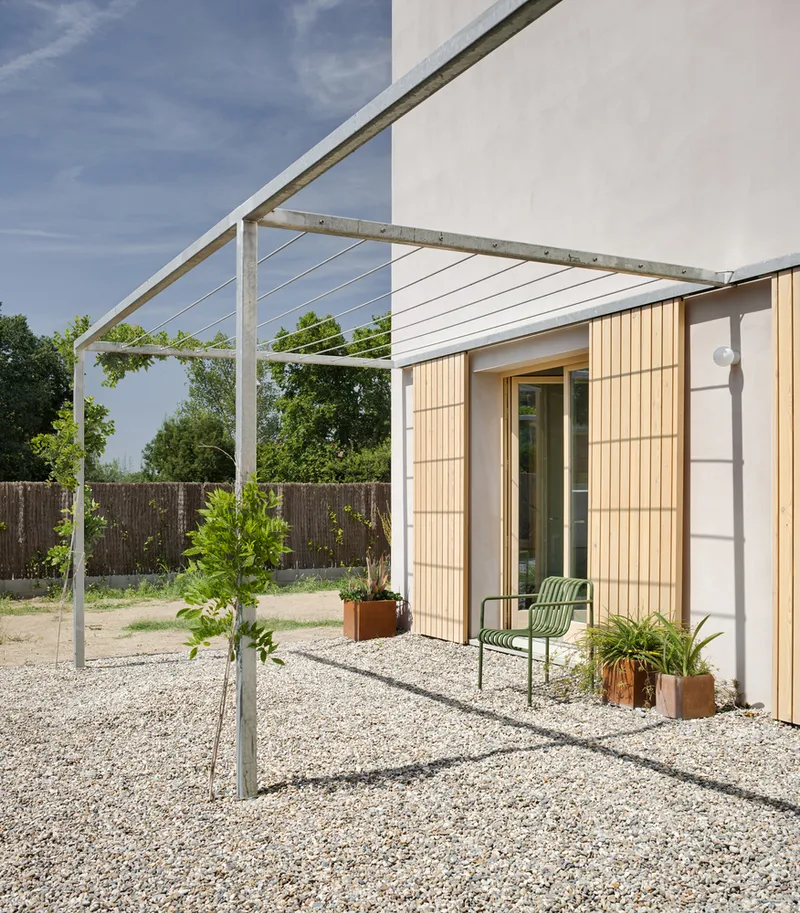 Steel pergola with cable railings over a gravel courtyard with potted plants and a green chair